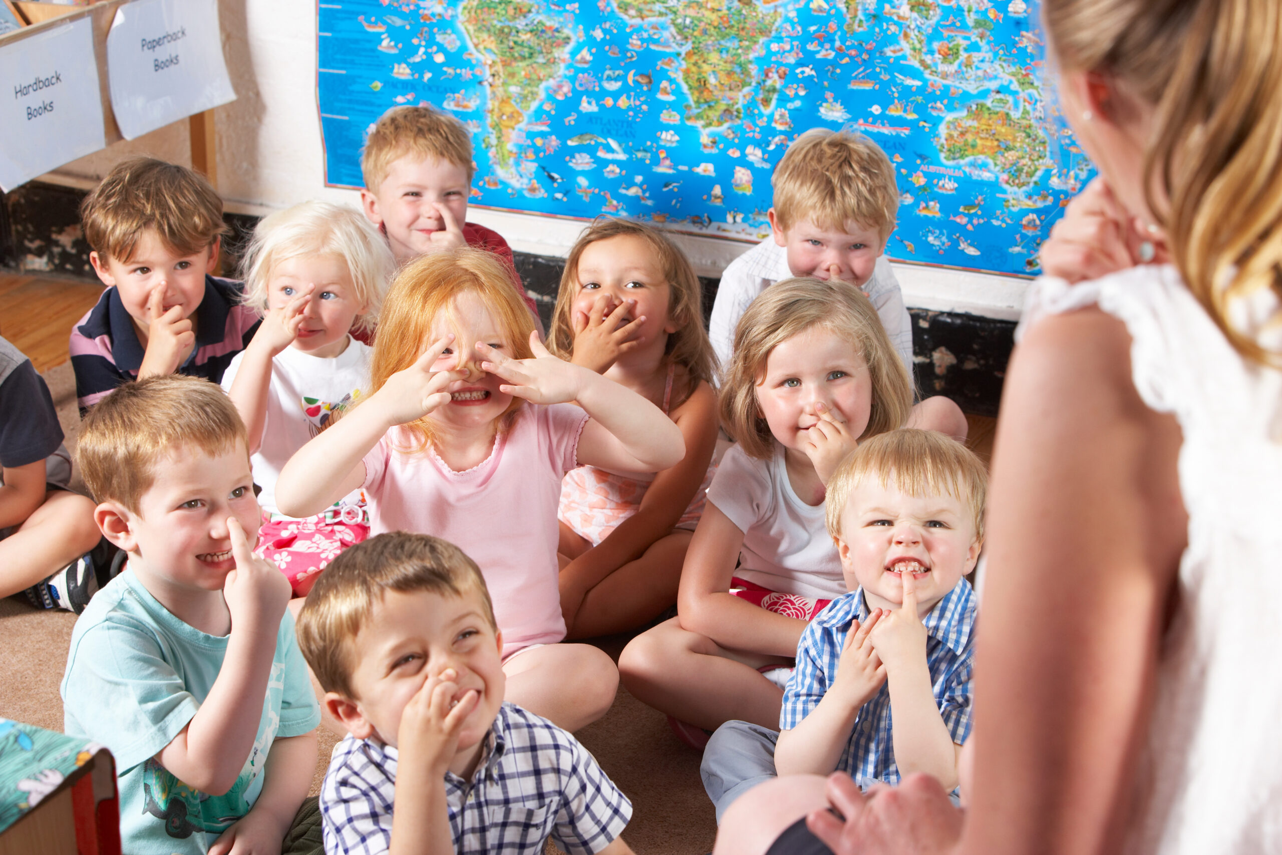 Un gruppo di bambini seduti a terra imita i gesti dell'insegnante durante la propedeutica musicale
